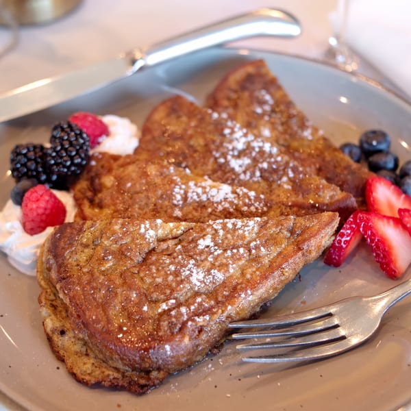 Golden French toast triangles dusted with powdered sugar, served with fresh berries and whipped cream.