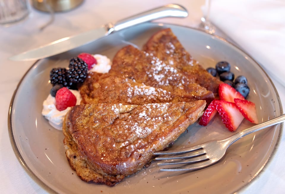 Golden French toast triangles dusted with powdered sugar, served with fresh berries and whipped cream.