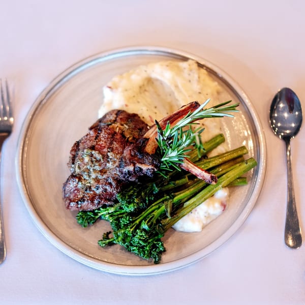 Grilled lamb chops with mashed potatoes, broccolini, and rosemary on a white plate.