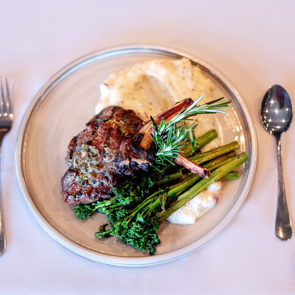Grilled lamb chops with mashed potatoes, broccolini, and rosemary on a white plate.