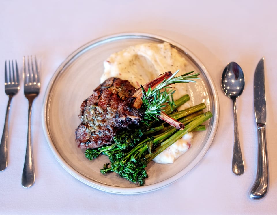 Grilled lamb chops with mashed potatoes, broccolini, and rosemary on a white plate.