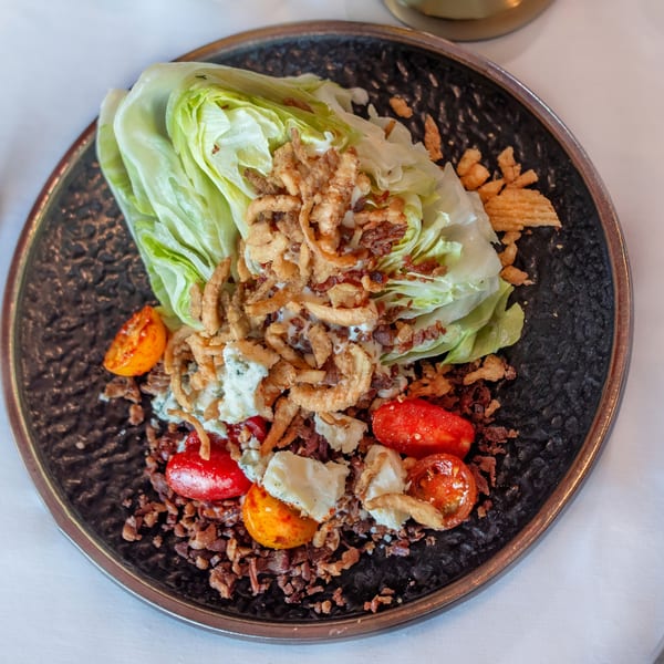 Wedge salad with blue cheese, bacon, fried onions, and cherry tomatoes on a dark plate.