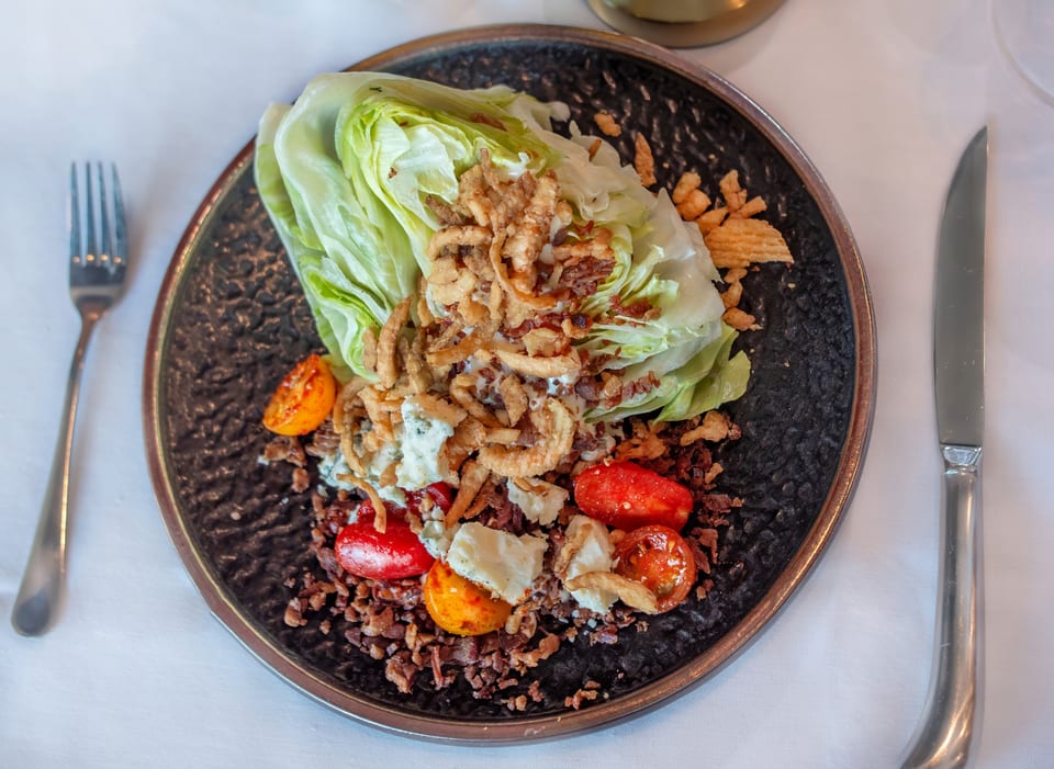Wedge salad with blue cheese, bacon, fried onions, and cherry tomatoes on a dark plate.