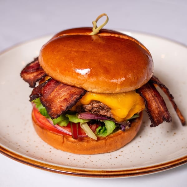 Gourmet bacon cheeseburger with lettuce, tomato, and onion on a brioche bun, served on a white plate.