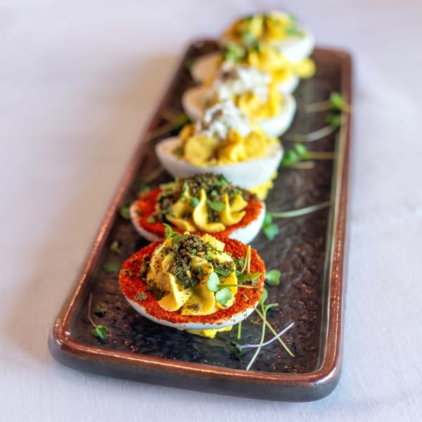 A platter of deviled eggs, some garnished with paprika and herbs, others with white cream.