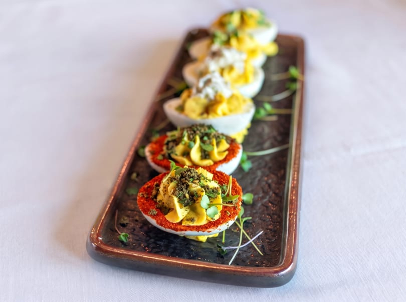 A platter of deviled eggs, some garnished with paprika and herbs, others with white cream.