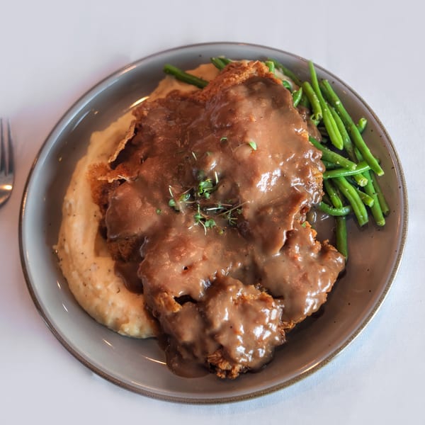Chicken fried steak with gravy, mashed potatoes, and green beans on a gray plate with a fork.