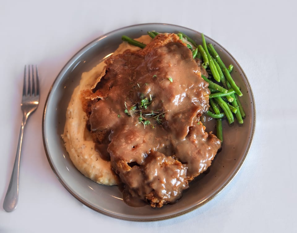 Chicken fried steak with gravy, mashed potatoes, and green beans on a gray plate with a fork.
