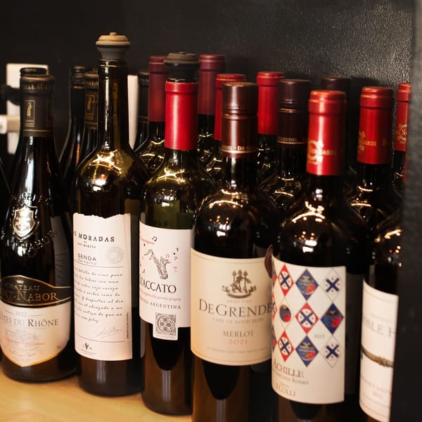 A close-up view of various wine bottles with different labels and red foil tops on a shelf.