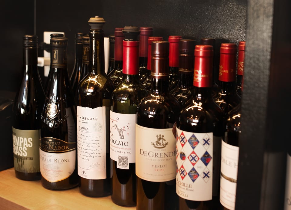 A close-up view of various wine bottles with different labels and red foil tops on a shelf.