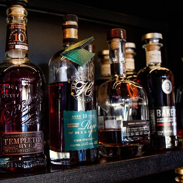 A close-up of various whiskey and bourbon bottles, including Templeton Rye, on a dark shelf.