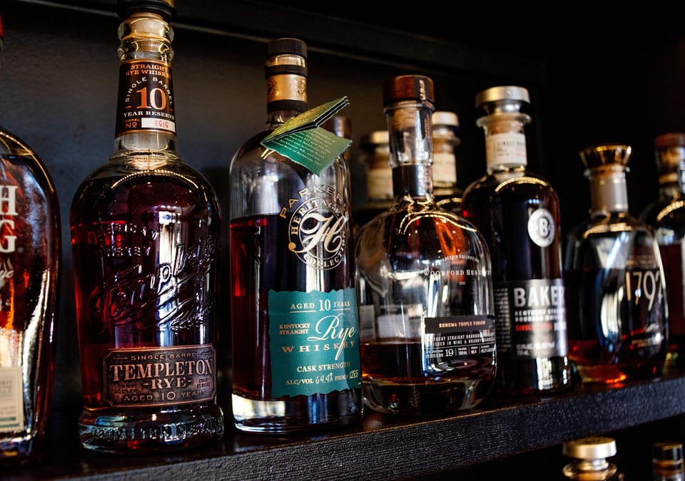 A close-up of various whiskey and bourbon bottles, including Templeton Rye, on a dark shelf.