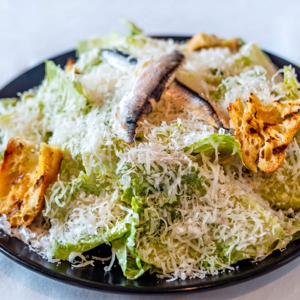 Caesar salad with anchovies, croutons, and shredded Parmesan cheese on a black plate.