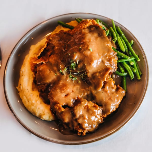Chicken fried steak with gravy, mashed potatoes, and green beans on a plate with a fork.