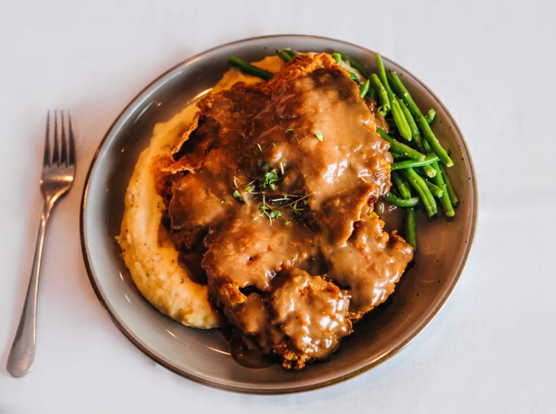 Chicken fried steak with gravy, mashed potatoes, and green beans on a plate with a fork.