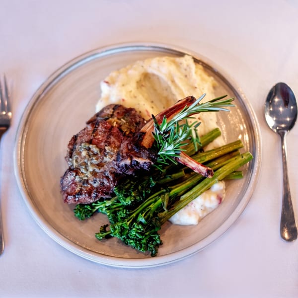 Grilled lamb chops with mashed potatoes, broccolini, and rosemary on a white tablecloth.