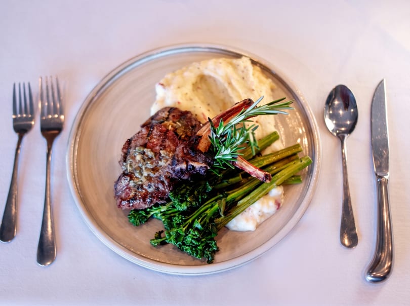 Grilled lamb chops with mashed potatoes, broccolini, and rosemary on a white tablecloth.