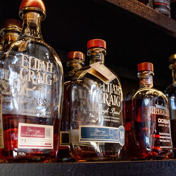 Several bottles of Elijah Craig and Jefferson's Ocean bourbon whiskey are displayed on a dark shelf.