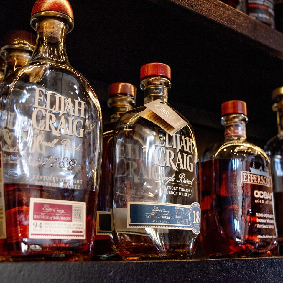 Several bottles of Elijah Craig and Jefferson's Ocean bourbon whiskey are displayed on a dark shelf.