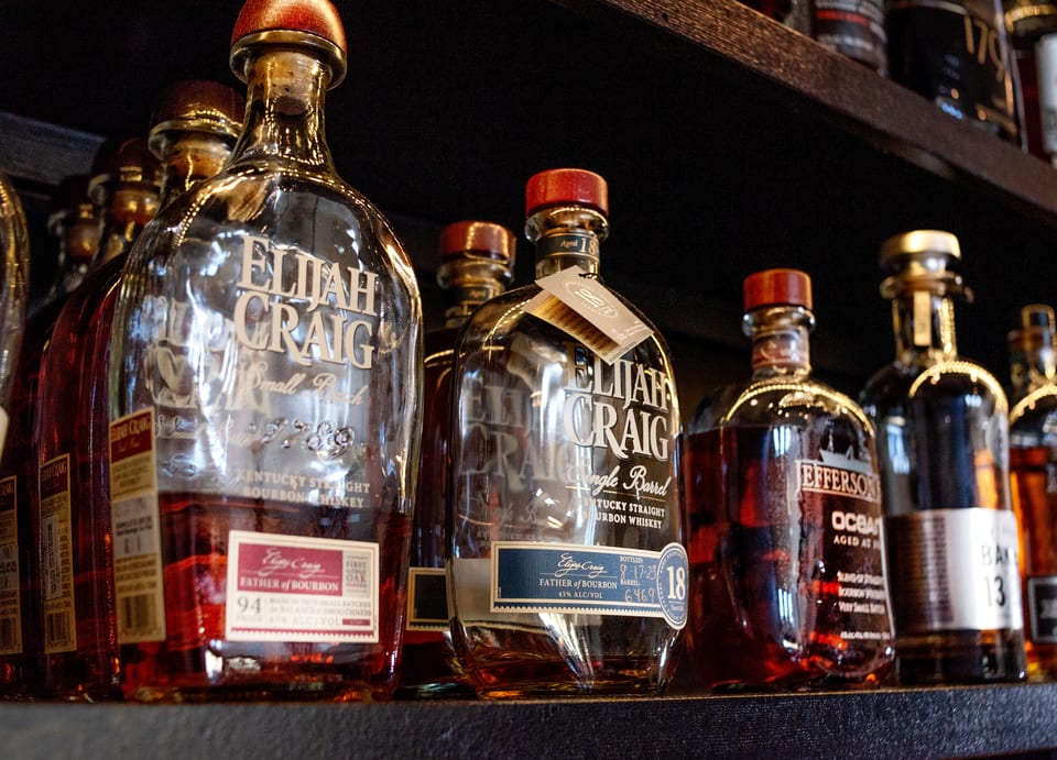 Several bottles of Elijah Craig and Jefferson's Ocean bourbon whiskey are displayed on a dark shelf.