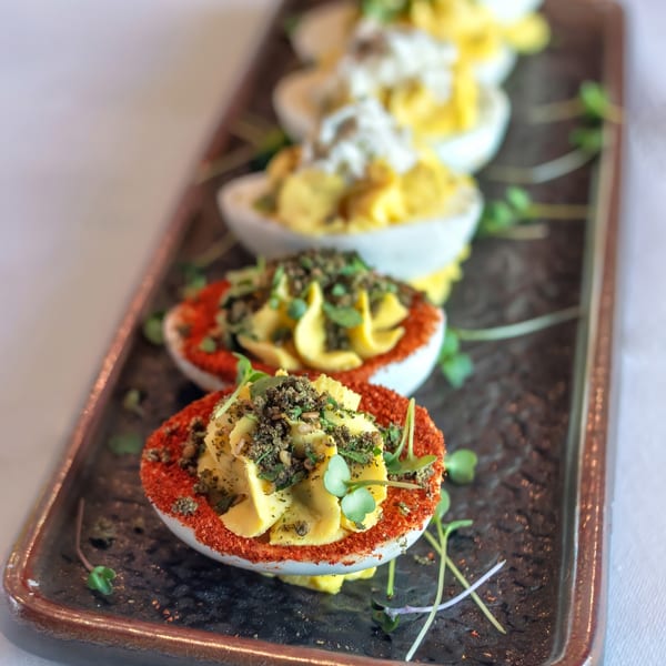 A rectangular platter holds five deviled eggs, two with red paprika and green herbs, three with white topping.