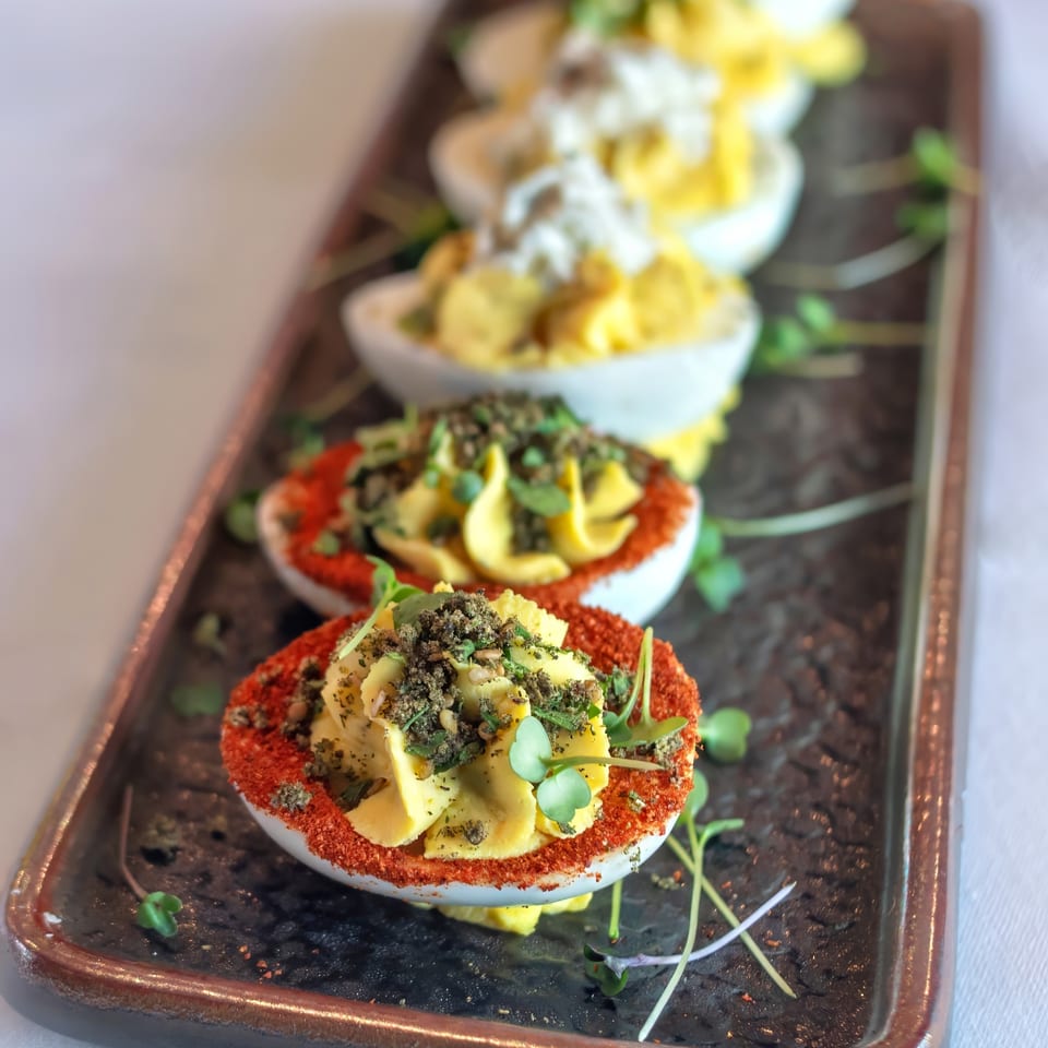 A rectangular platter holds five deviled eggs, two with red paprika and green herbs, three with white topping.
